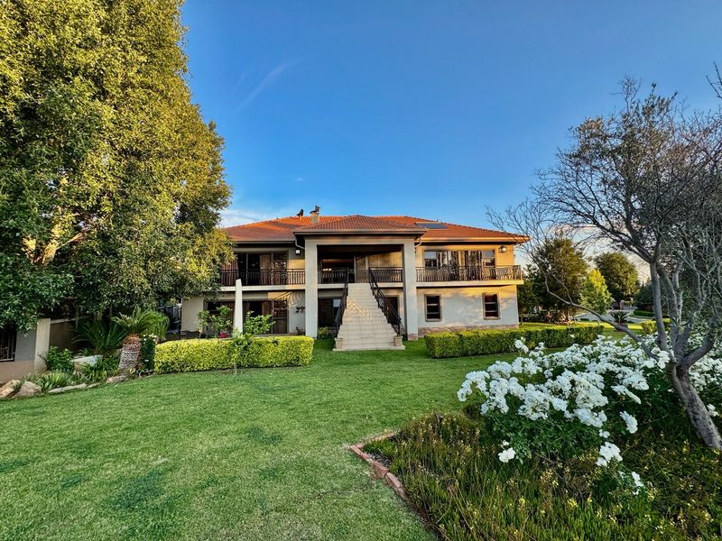 A well-maintained double-story residence featuring a central staircase, expansive upper balcony with wrought iron railings, and a beautifully landscaped rear garden.