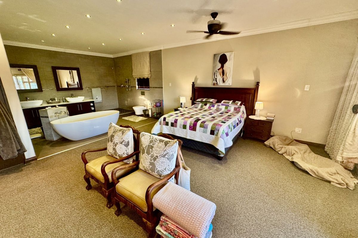 Spacious open-plan bedroom featuring an integrated en-suite bathroom with a modern freestanding bathtub and double vanity, complemented by recessed lighting and a ceiling fan.