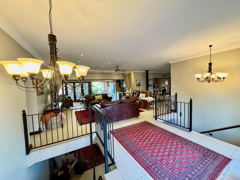 Spacious open-plan living area featuring tiled flooring, recessed lighting, and a decorative wrought iron balustrade overlooking the staircase.
