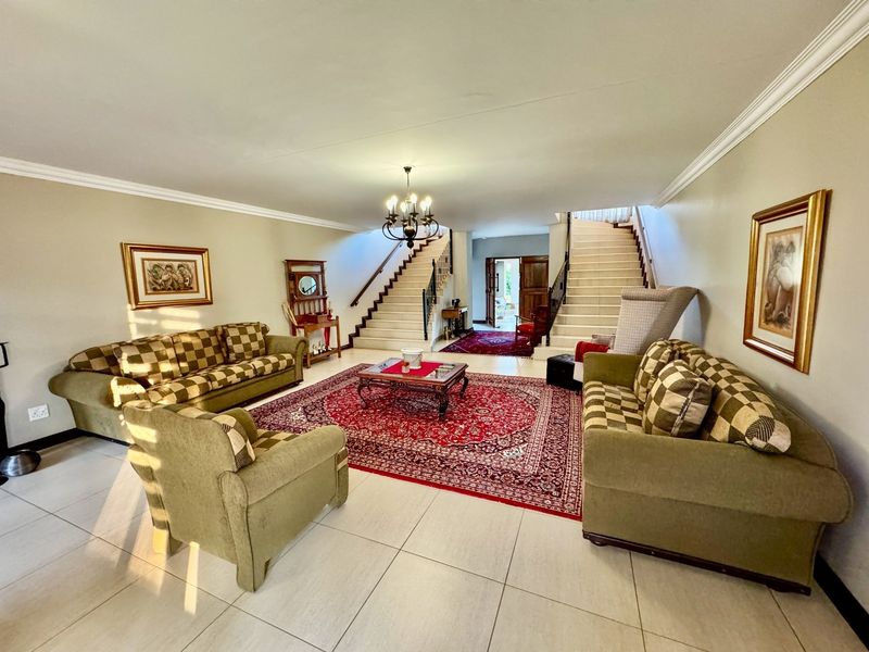 Spacious living room featuring dual staircases with wrought iron balustrades, tiled flooring, and elegant crown molding, creating a grand entrance and seating area.