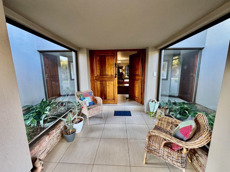 A welcoming entrance foyer featuring tiled flooring, large glass panels overlooking internal planter boxes, and a solid timber double door leading into the home.