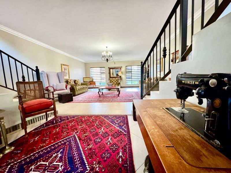 Spacious open-plan living area featuring tiled flooring, a staircase with metal balustrades, and large windows with venetian blinds.
