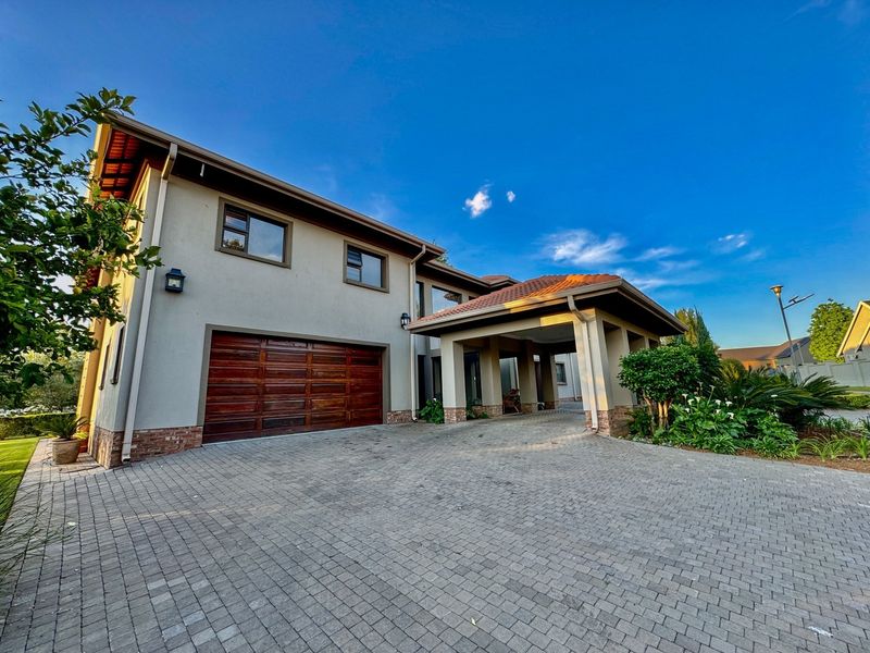 A well-maintained front exterior featuring a paved driveway, a double garage, and a covered entrance portico with attractive brick and plaster finishes.