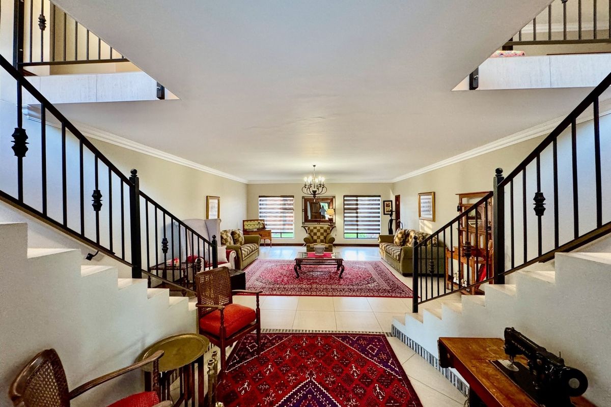 Spacious living area featuring a symmetrical dual staircase with wrought iron balustrades, tiled flooring, and elegant cove cornicing.