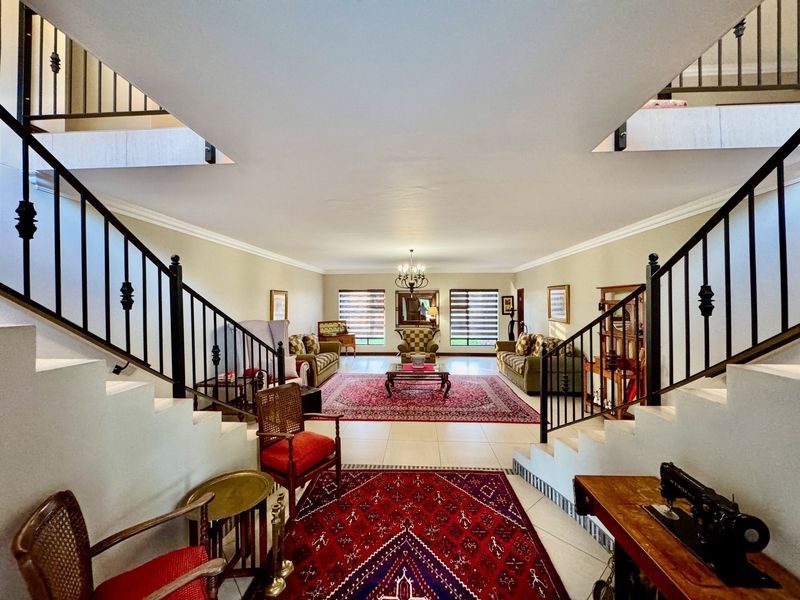 Spacious living area featuring a symmetrical dual staircase with wrought iron balustrades, tiled flooring, and elegant cove cornicing.