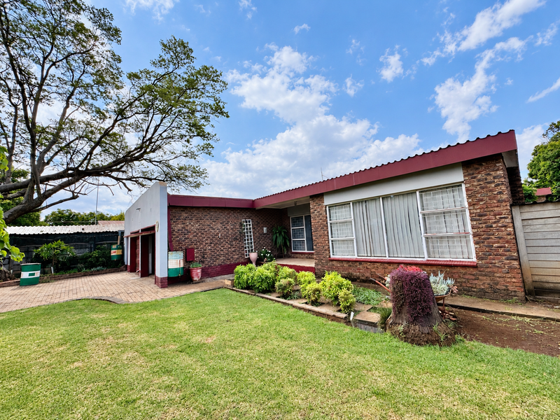 Rear view of a face brick house featuring a paved patio area, established lawn, and mature trees under a clear sky.