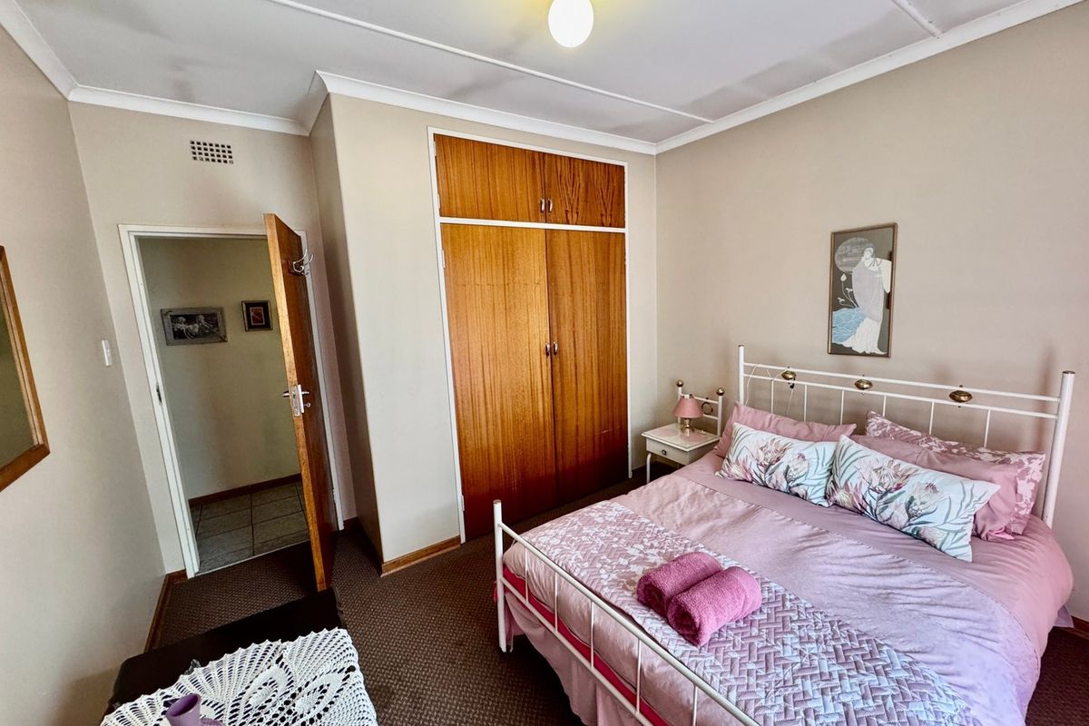 A functional bedroom featuring a built-in wooden wardrobe, neutral wall finishes, and carpeted flooring.