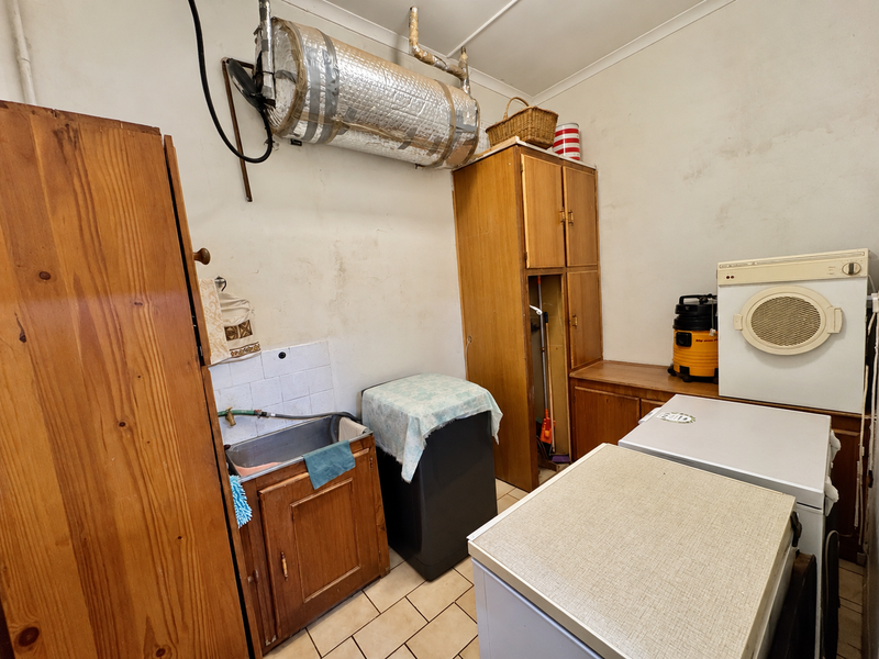 A functional laundry room featuring built-in wooden cabinetry, a utility sink, and tiled flooring, with a wall-mounted geyser and ample storage space.
