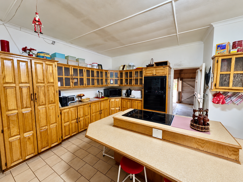 A spacious kitchen featuring extensive wooden cabinetry, a central island with a built-in electric cooktop, and tiled flooring.