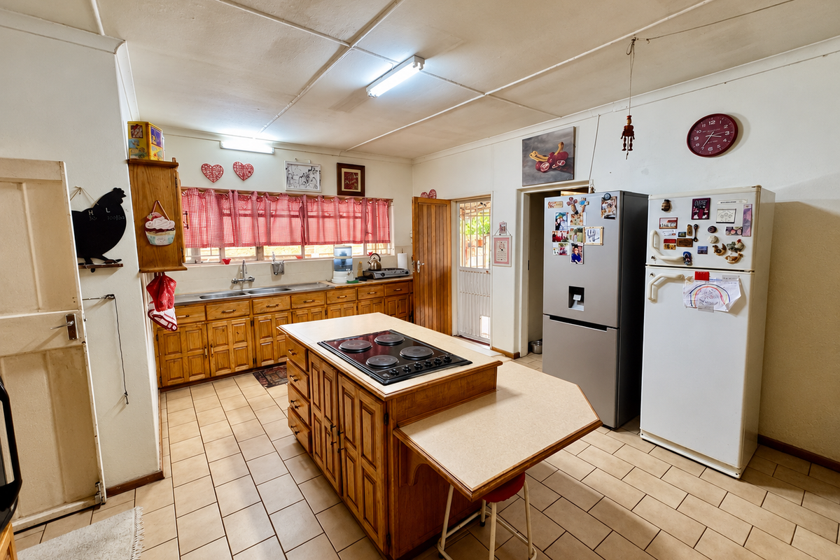 A functional kitchen featuring wooden cabinetry, a central island with a built-in hob, double sink, and tiled flooring, offering a traditional layout.