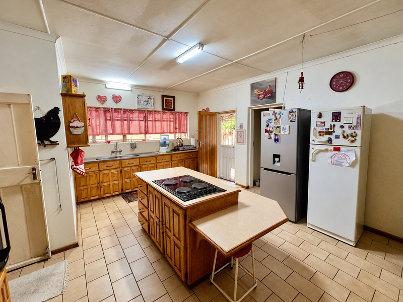A functional kitchen featuring wooden cabinetry, a central island with a built-in hob, double sink, and tiled flooring, offering a traditional layout.