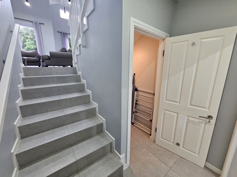 A bright hallway featuring a modern tiled staircase with a white balustrade and access to an under-stair storage cupboard.