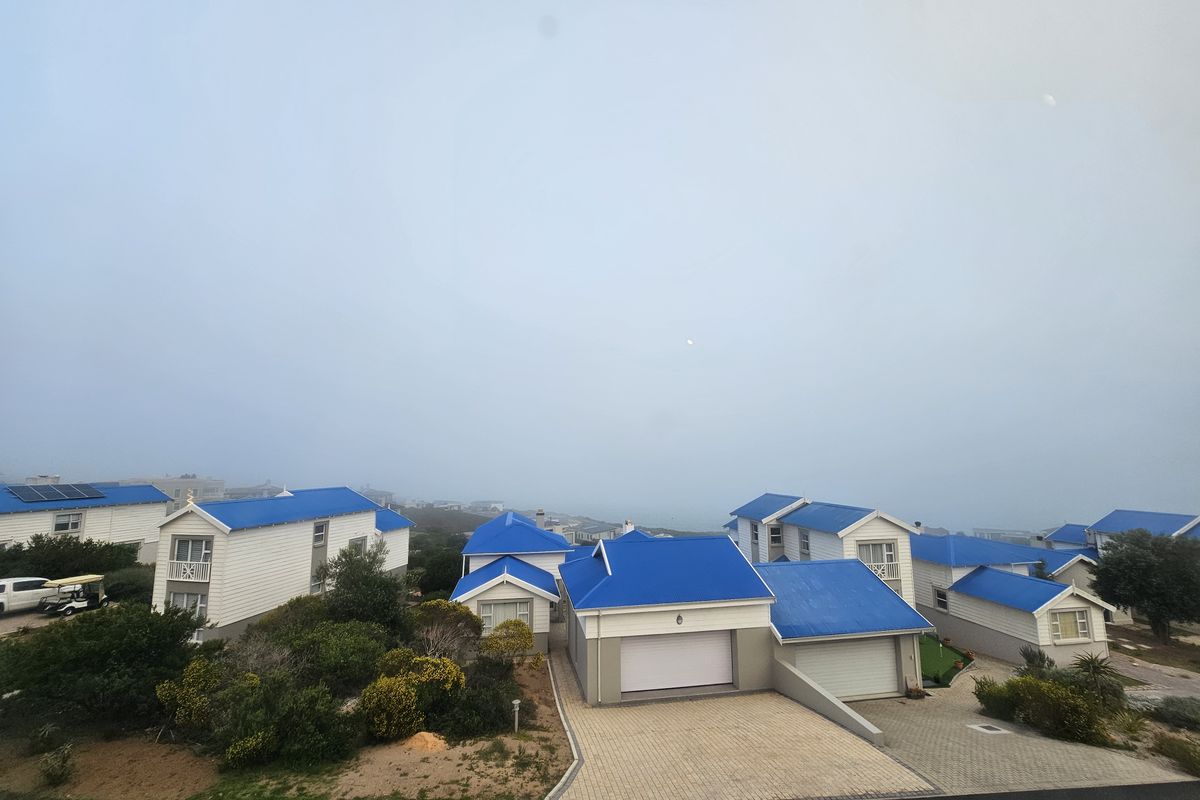An elevated aerial view of a residential townhouse complex featuring blue metal roofs, paved driveways, and integrated garages within a coastal estate setting.