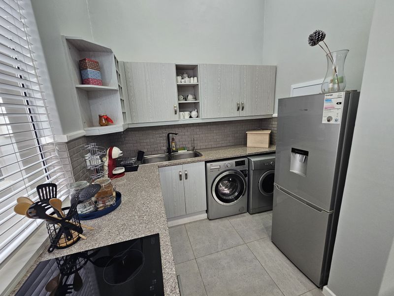 A functional scullery featuring built-in cabinetry, granite countertops, subway tile backsplash, and dedicated space for laundry appliances and a refrigerator.