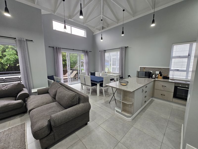 Spacious open-plan living and kitchen area featuring vaulted ceilings with exposed rafters, granite island, modern tiled flooring, and direct access to an outdoor deck.