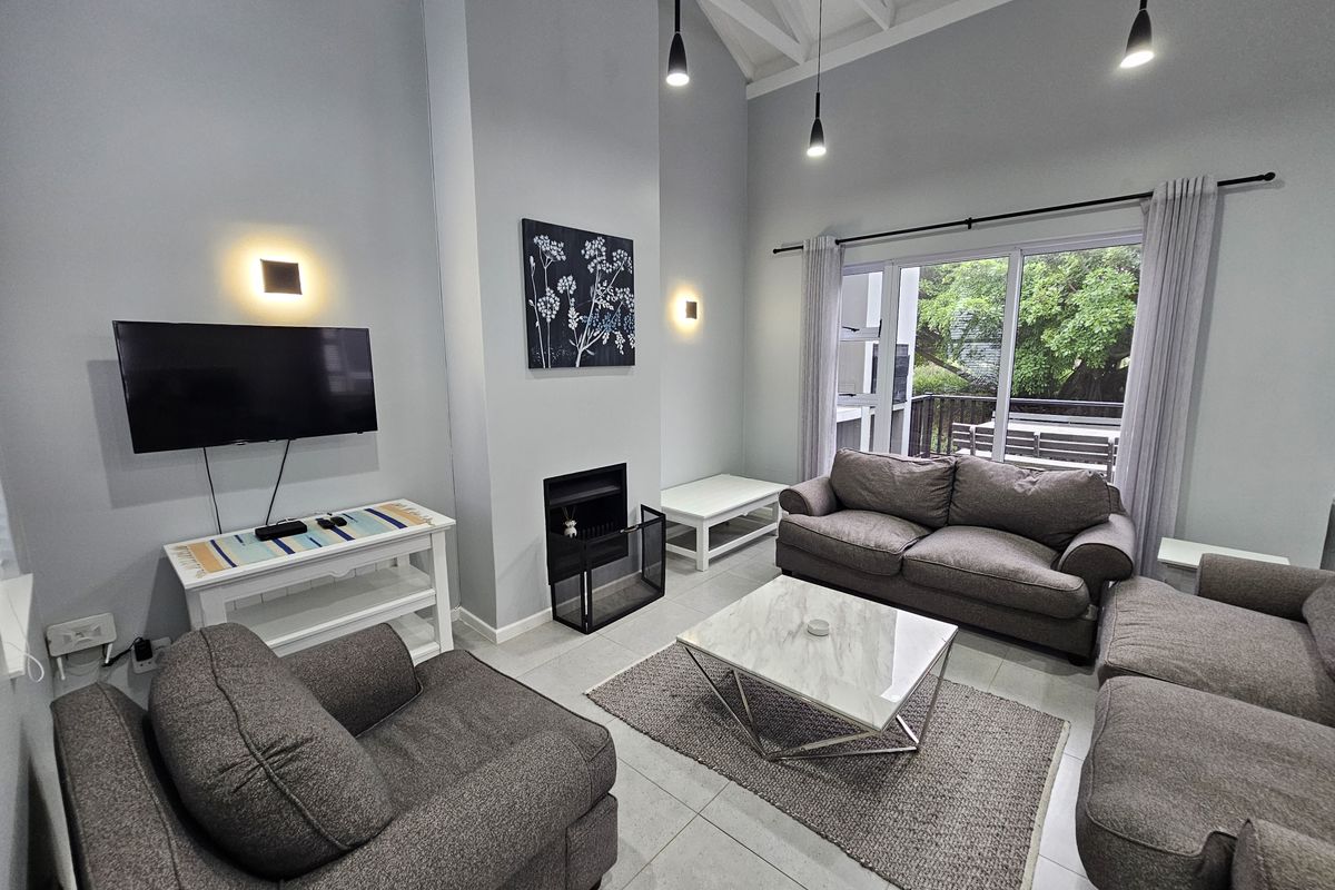 Spacious living room featuring a high vaulted ceiling, built-in fireplace, tiled floors, and large sliding glass doors providing access to an outdoor balcony.