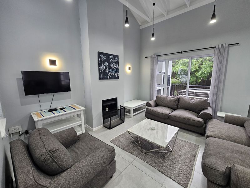Spacious living room featuring a high vaulted ceiling, built-in fireplace, tiled floors, and large sliding glass doors providing access to an outdoor balcony.
