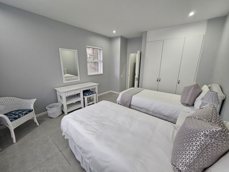 A well-maintained bedroom featuring neutral grey walls, tiled flooring, built-in cupboards, and recessed lighting, offering a clean and functional living space.