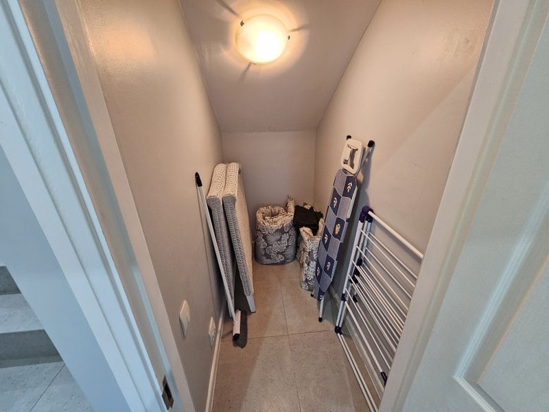 A compact under-stair utility storage space featuring tiled flooring and a ceiling light fixture, suitable for general household storage.