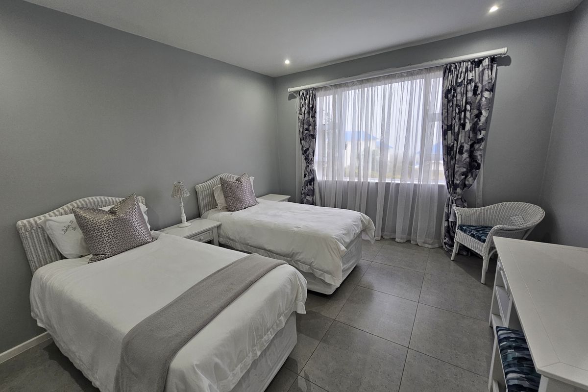 A well-maintained bedroom featuring neutral grey walls, large windows with curtain tracks, and modern tiled flooring.