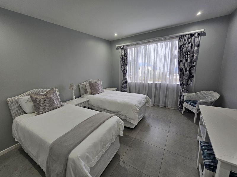 A well-maintained bedroom featuring neutral grey walls, large windows with curtain tracks, and modern tiled flooring.