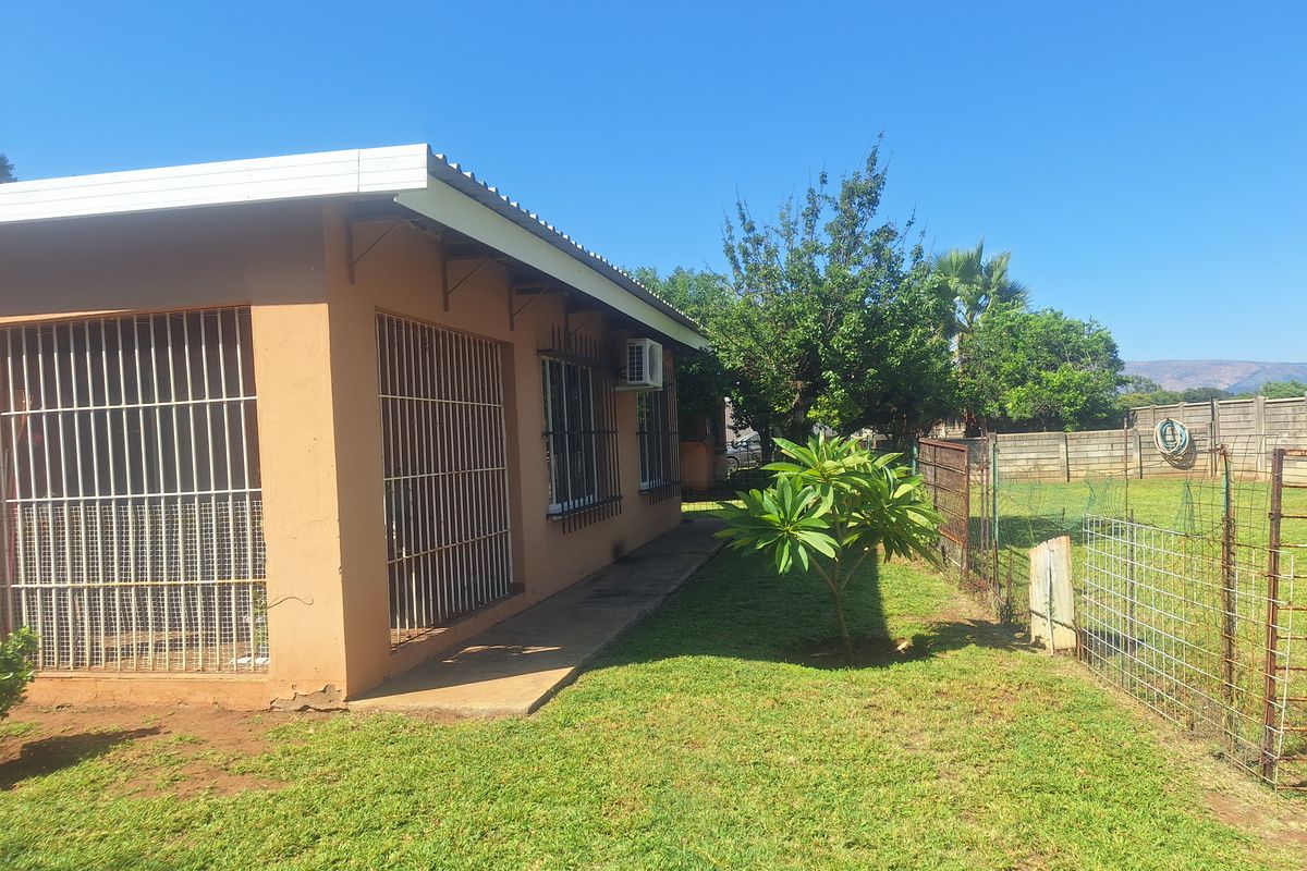Rear exterior view of the farm dwelling featuring a covered patio area, security bars on windows, and an established garden with perimeter fencing.
