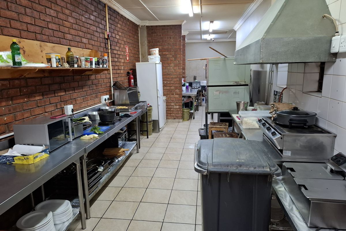 A functional commercial kitchen featuring stainless steel work surfaces, a large extractor hood, tiled flooring, and exposed brick walls.