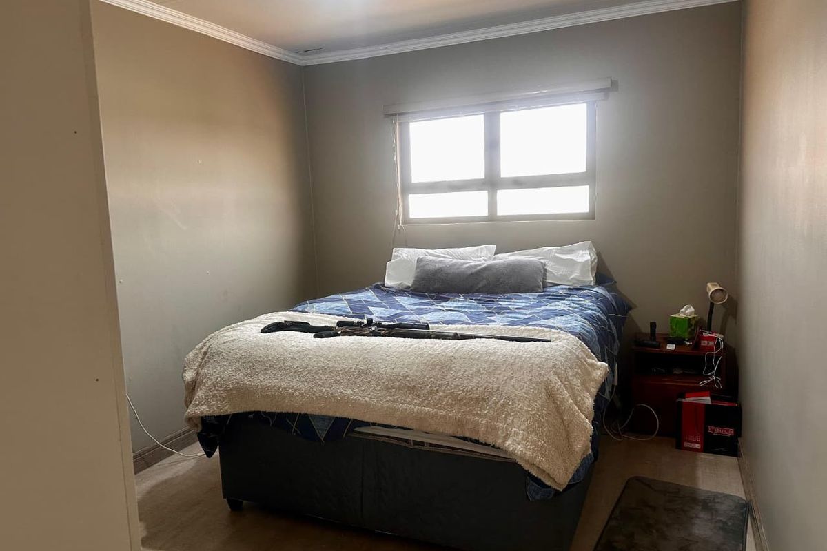 A functional bedroom featuring neutral wall tones, crown molding, and a window providing natural light.