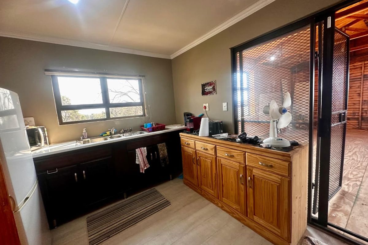 A functional kitchen area featuring dark lower cabinetry, a stainless steel sink, and a secondary wooden storage unit, adjacent to a screened-in utility space.