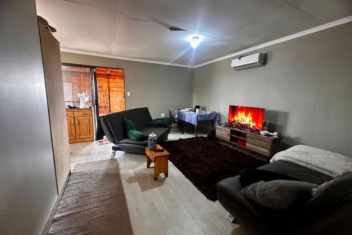 A spacious living room featuring light-toned flooring, a wall-mounted air conditioning unit, and direct access to an adjoining outdoor area.