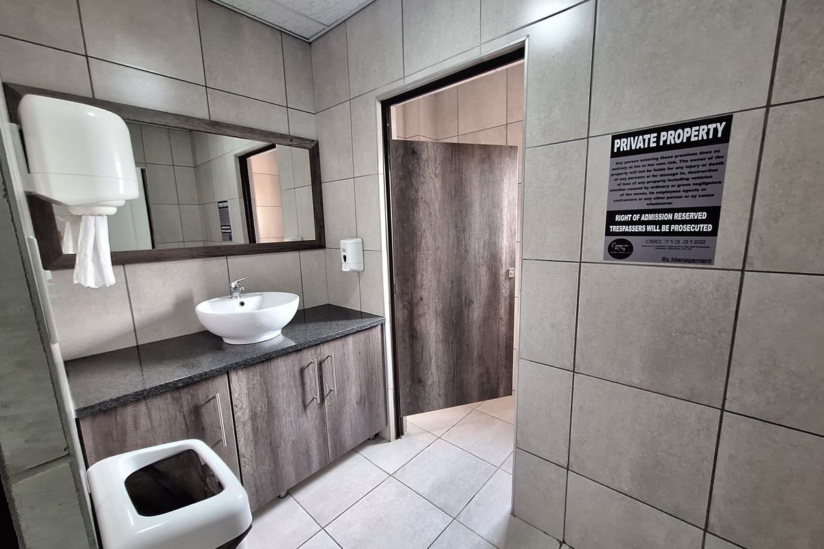 Commercial restroom featuring a modern vanity with a vessel sink, granite countertop, wood-look cabinetry, and full-height wall tiling.
