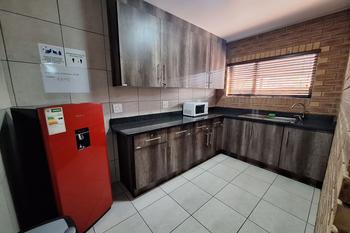 A functional commercial kitchen area featuring dark wood-grain cabinetry, granite countertops, a stainless steel sink, and tiled flooring.