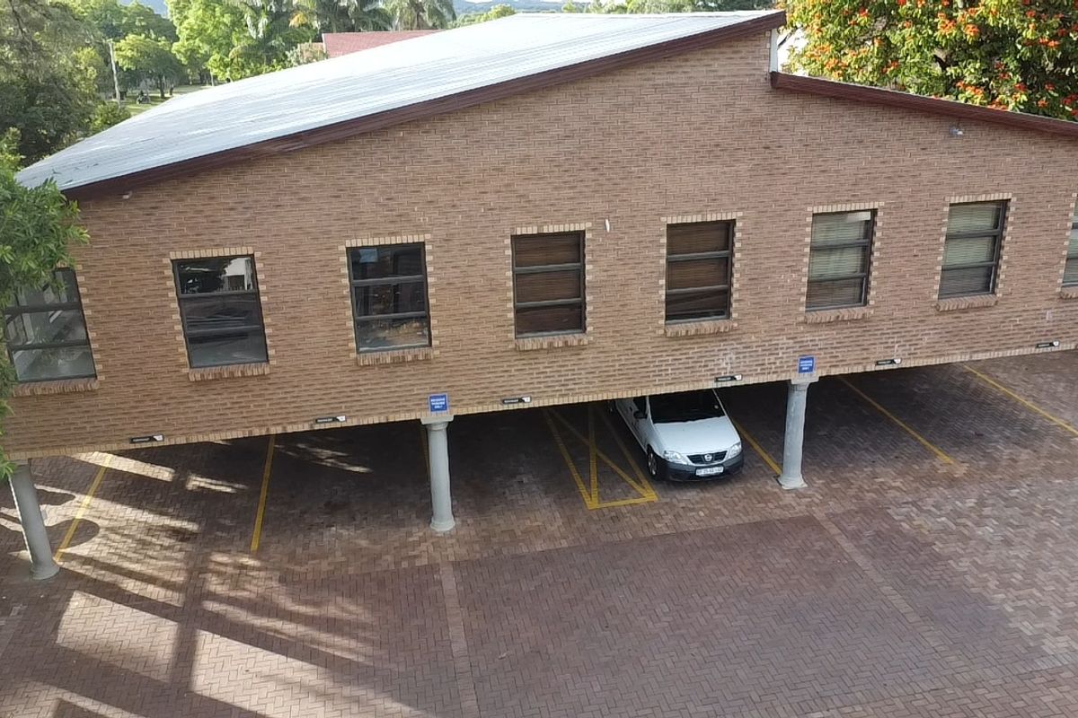 Aerial view of a commercial building featuring a brick facade, pitched roof, and a covered ground-level parking area with paved driveway.