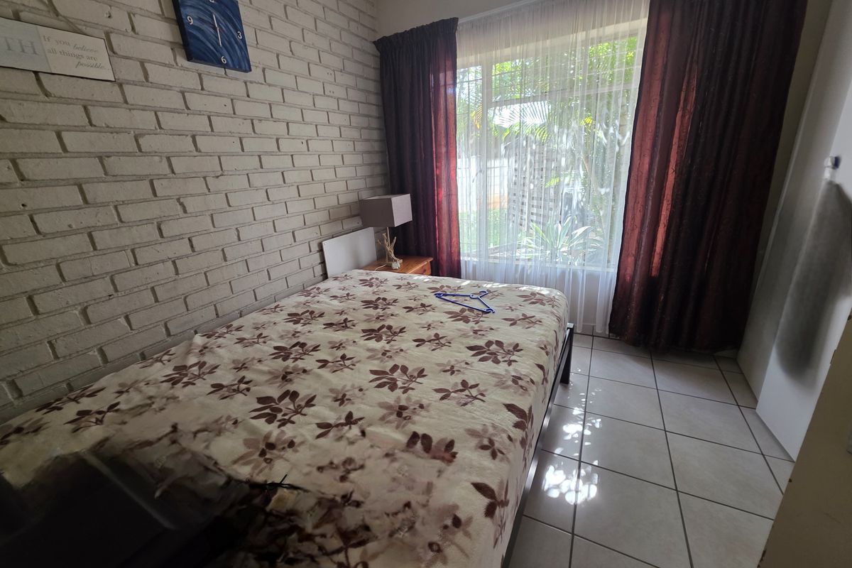 A bedroom featuring a textured brick feature wall, tiled flooring, and large window with curtains allowing natural light.