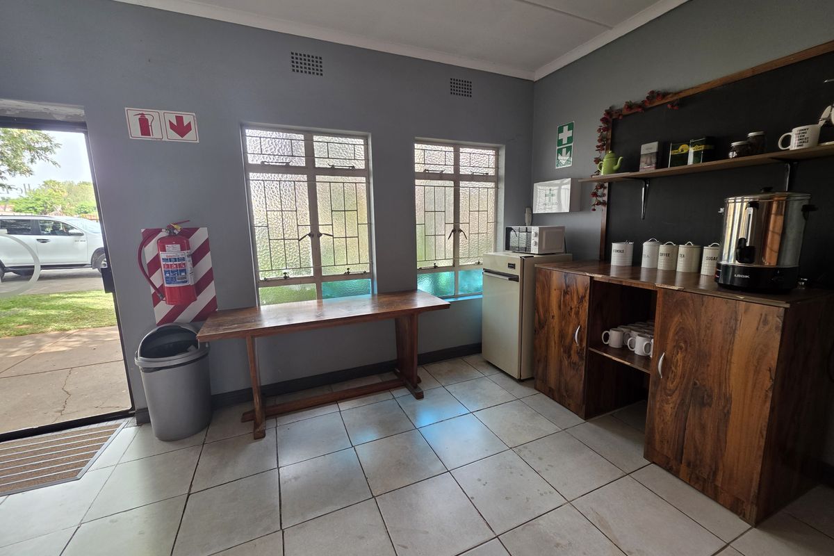 A functional commercial kitchenette area featuring tiled flooring, built-in wooden cabinetry, and direct access to the exterior.