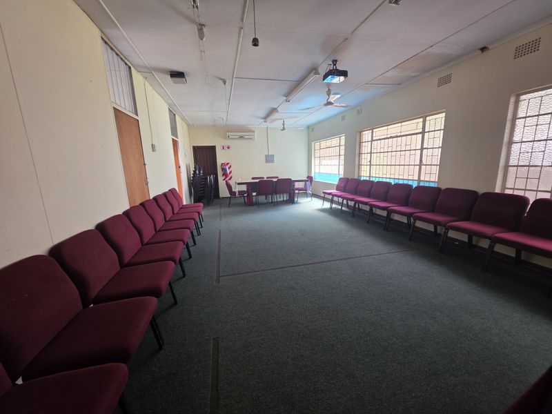 A functional commercial meeting or conference room featuring carpeted flooring, large windows for natural light, and a ceiling-mounted projector.