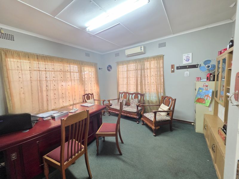 A functional office space featuring large windows with curtains, wall-mounted air conditioning unit, and carpeted flooring.