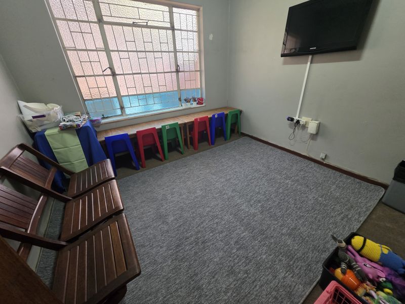 A functional office or utility space featuring a large window with security bars, grey carpeting, and wall-mounted electrical and television connections.