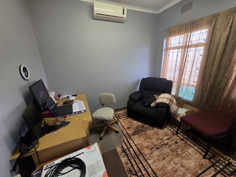 A functional office space featuring a wall-mounted air conditioning unit and a window with security bars.