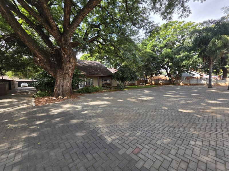 Spacious paved driveway and parking area featuring mature trees and established landscaping, providing ample exterior space for commercial use.