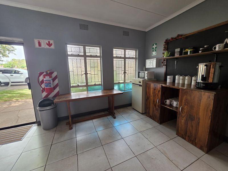 A functional commercial kitchenette area featuring tiled flooring, built-in wooden cabinetry, and direct access to the exterior.