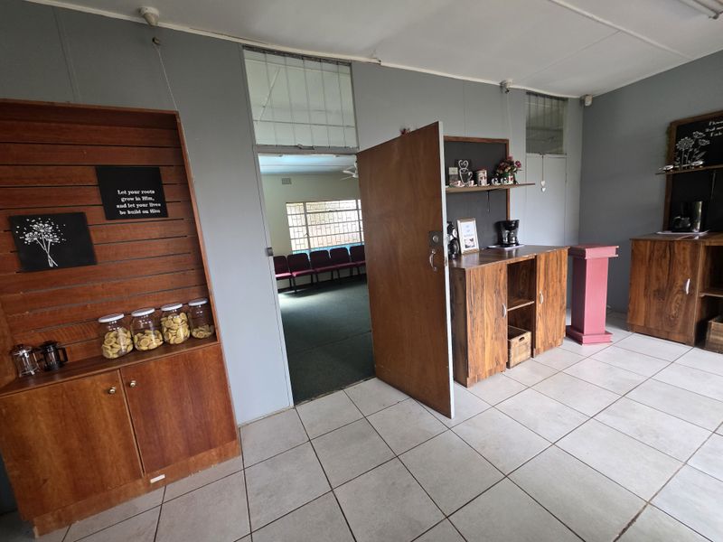 A functional commercial interior space featuring tiled flooring, built-in wooden cabinetry, and a doorway leading to an adjacent room with carpeted flooring.
