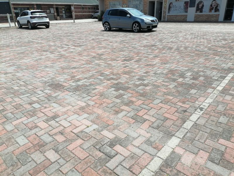 A paved commercial parking area fronting a brick-faced retail building with storefront access.