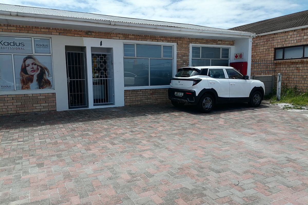 Front exterior view of a commercial property featuring a brick facade, paved parking area, and secure entrance with security gates.
