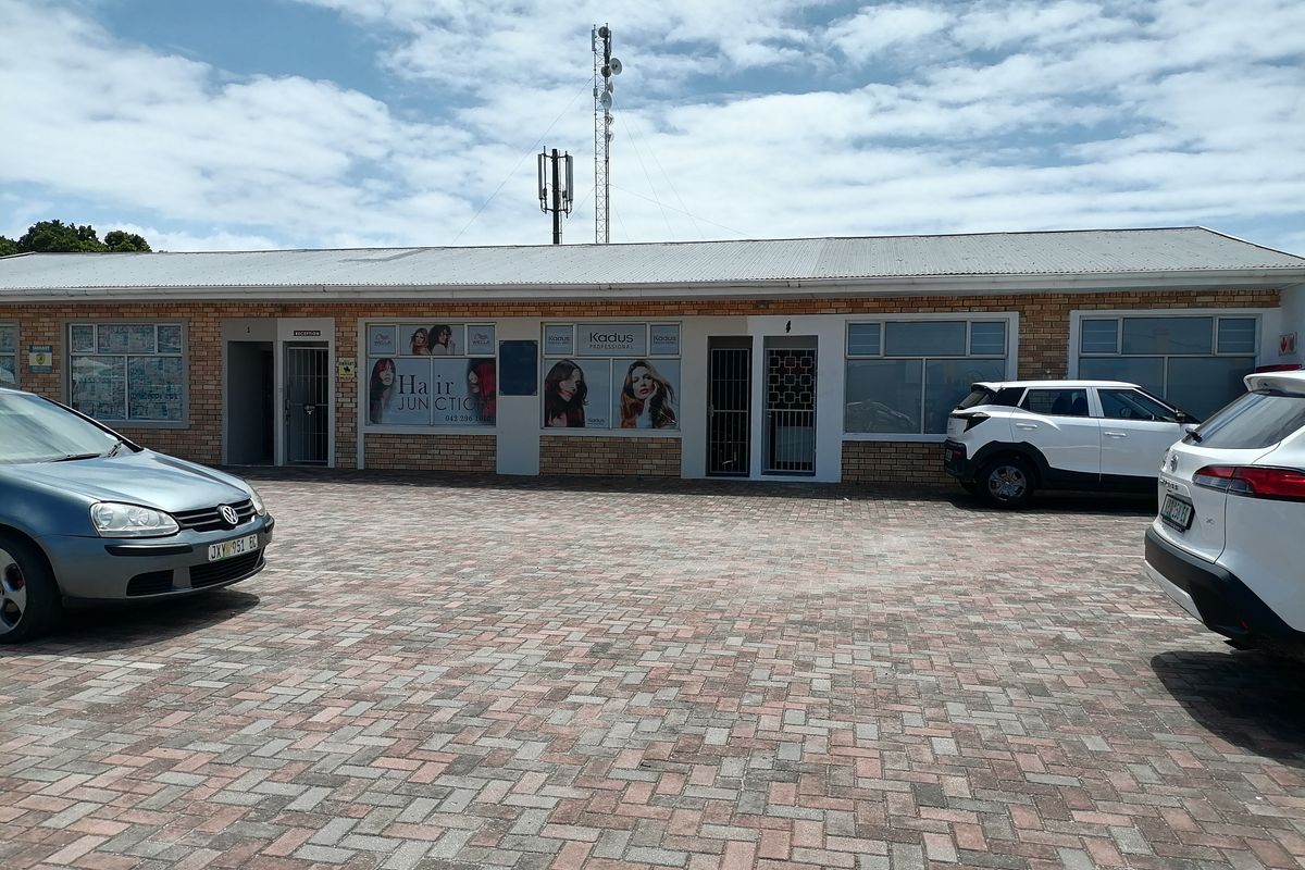 Front exterior view of a commercial strip building featuring a brick facade, paved parking area, and multiple business entrances with security gates.