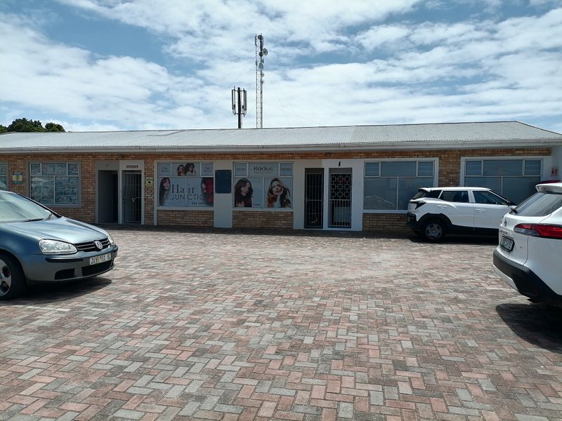 Front exterior view of a commercial strip building featuring a brick facade, paved parking area, and multiple business entrances with security gates.
