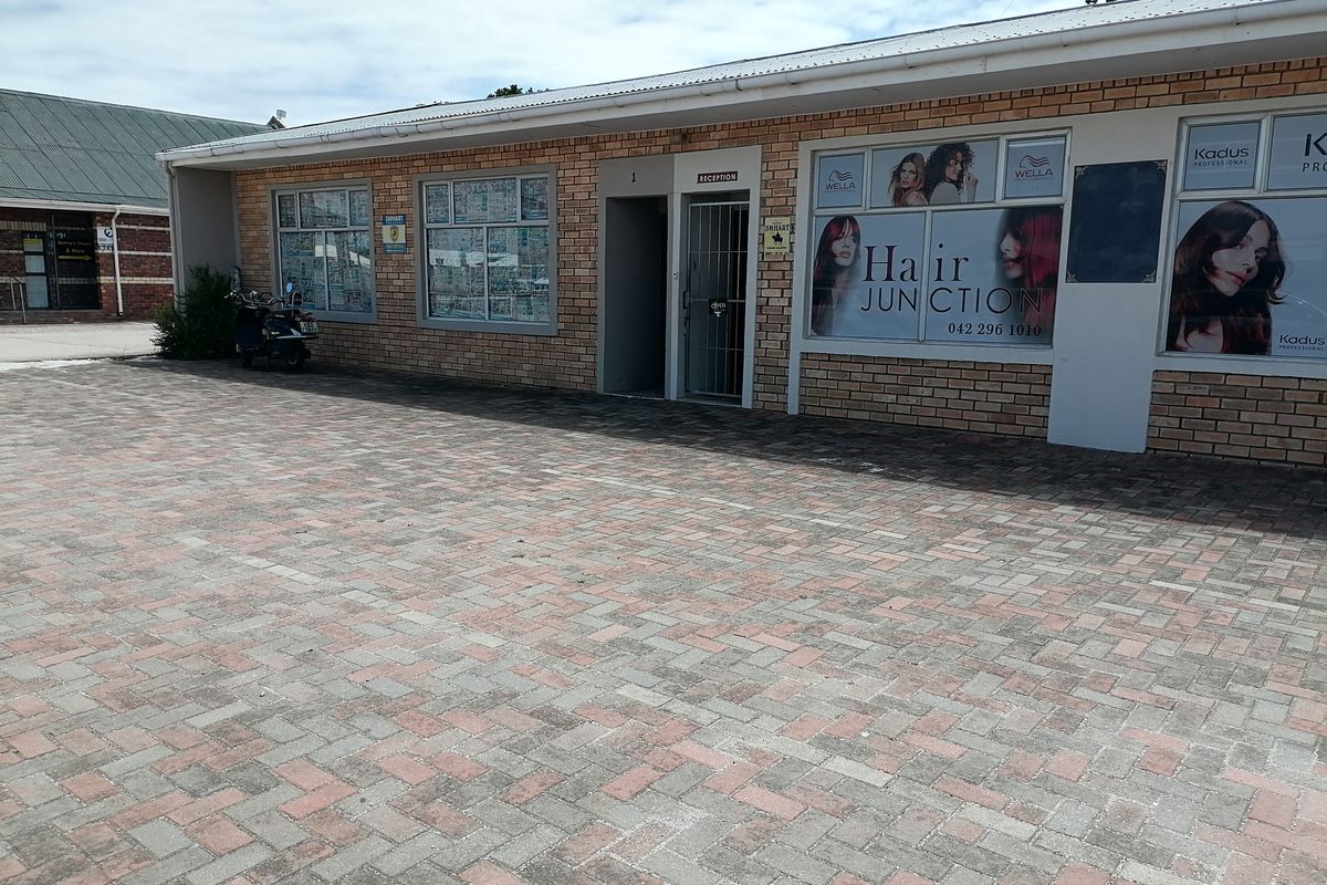 Front exterior view of a commercial property featuring a brick facade, paved parking area, and large display windows currently occupied by a hair salon.