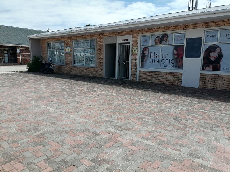 Front exterior view of a commercial property featuring a brick facade, paved parking area, and large display windows currently occupied by a hair salon.
