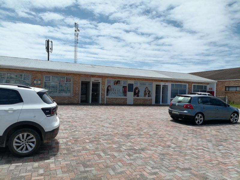 Front exterior view of a commercial brick building featuring a paved parking area, large display windows, and security gates at the entrances.
