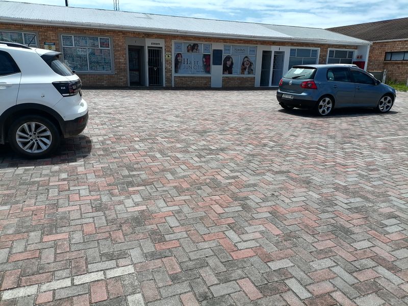 Front exterior view of a commercial building featuring a brick facade, metal roofing, and a paved parking area.
